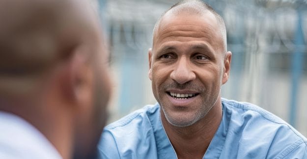 Smiling man in a blue scrubs shirt having a conversation outdoors