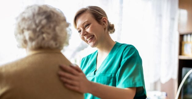 Smiling caregiver comforting an elderly person indoors.